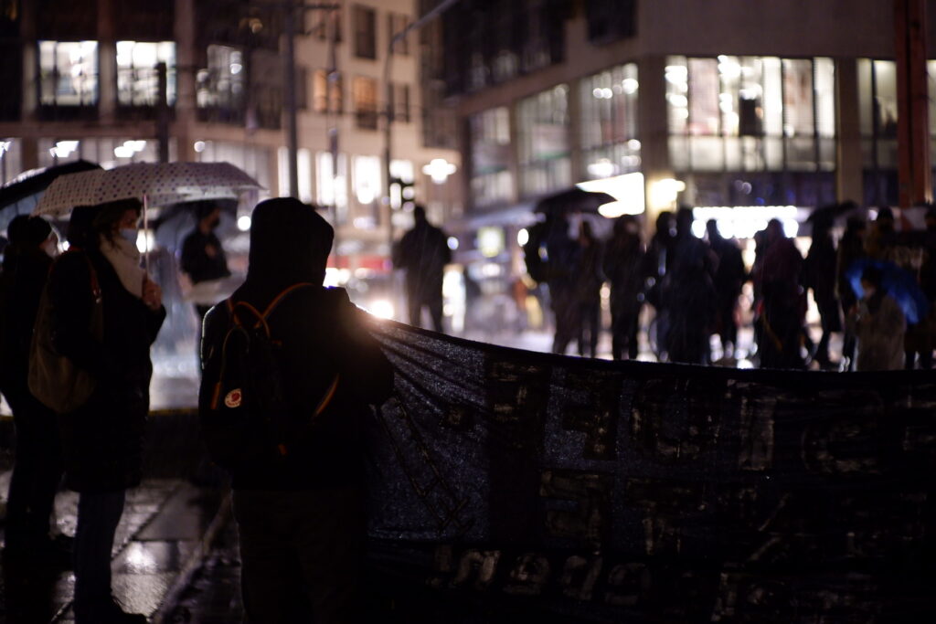 Personen auf einer Demonstration halten ein Banner. Es ist dunkel.