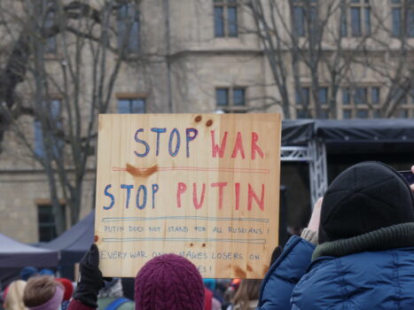 Eine Person hält auf einer Demonstration ein Schild hoch, auf dem "Stop War, Stop Putin" steht.