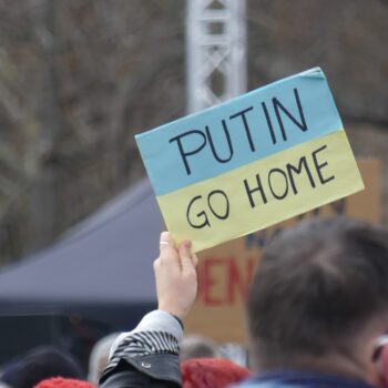 Eine Person hält ein Schild in den Farben der Ukrainischen Fahne hoch. Auf dem Schild steht Putin go home.